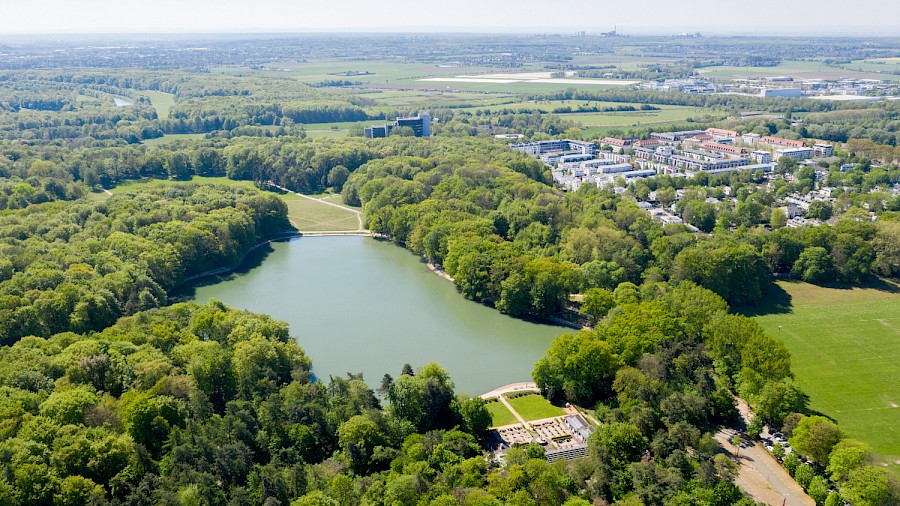 Blick über den Adenauer Weiher aus Richtung des Rhein-Energie-Stadions. Im Vordergrund der Club Astoria, rechts die Jahnwiesen. © Raimond Spekking / CC BY-SA 4.0 (via Wikimedia Commons) | Die Kölner Parkweiher – Adenauer Weiher